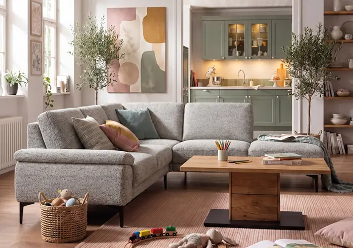 Graues Ecksofa mit Couchtisch, Spielzeug, Pflanzen und Küchenbereich im Hintergrund